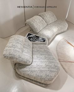 a couch and ottoman in a room with white walls, flooring and lighting on the ceiling