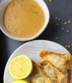 some food is on a white plate next to a bowl of soup and lemon wedges