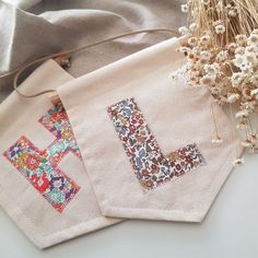 two cross - stitched letters are next to some dried flowers