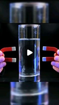 two hands holding red and white toothbrushes in front of a glass with water