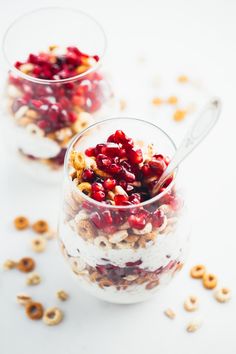 two glasses filled with granola and pomegranates on a white surface