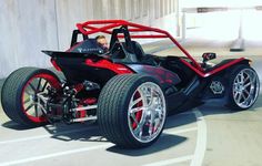 a man driving a red and black dune buggy on top of a parking lot