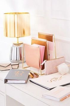 a white desk topped with notebooks and a lamp next to a book on top of a table