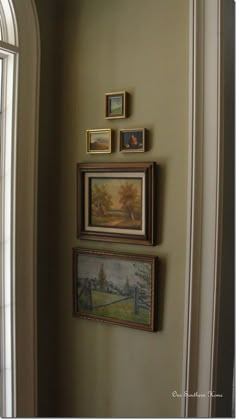 three framed pictures hang on the wall above a doorway with an arched window in the background