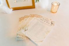 a close up of a menu on a table with a candle and some flowers in the background