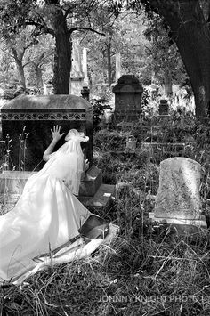 black and white photograph of a woman in a wedding dress sitting on the ground at a cemetery