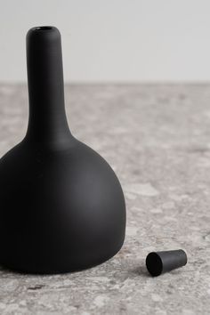 a black vase sitting on top of a table next to a small bottle with a tube sticking out of it