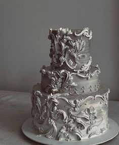 a three tiered wedding cake with intricate designs on the top and sides, sitting on a plate