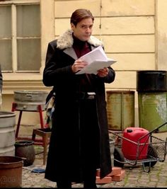 a woman standing in front of a building holding a piece of paper and looking at something