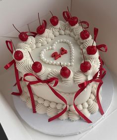 a heart shaped cake with cherries and ribbons around it on a white plate in a box