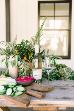 a table topped with cucumbers and bottles of wine next to a potted plant