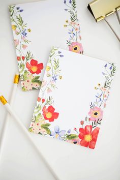 two notebooks with floral designs on them next to pens and markers, one is empty