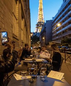 people sitting at tables in front of the eiffel tower with their cell phones