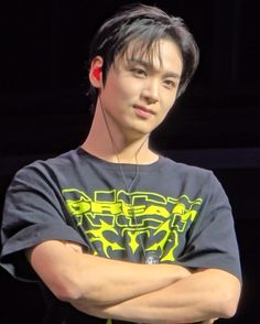 a young man with headphones on standing in front of a black background and looking at the camera