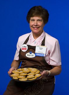 a woman in an apron holding a platter of donuts with stickers on them