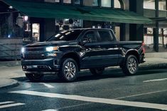 a black truck is parked on the side of the road at night in front of a building