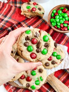 a person holding up a cookie with m & m candy on it next to other cookies