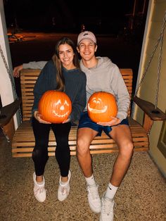 two people sitting on a bench holding pumpkins