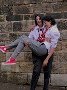 two people standing next to each other near a brick wall and one person is holding the woman's leg