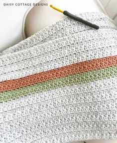 a crocheted blanket with an orange and green stripe on it next to a white wall