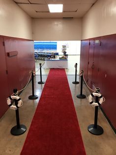 a red carpeted hallway leading to lockers with black and white barriers on each side