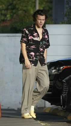 a man walking down the street in front of a black car and wearing yellow shoes