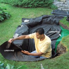 a man sitting on top of a black tarp in the middle of a garden