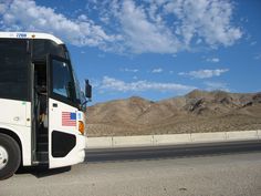 a white bus driving down the road with mountains in the backgrouds behind it