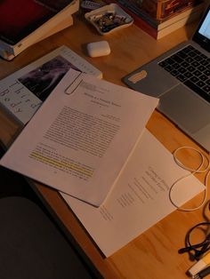 an open laptop computer sitting on top of a wooden desk next to papers and headphones