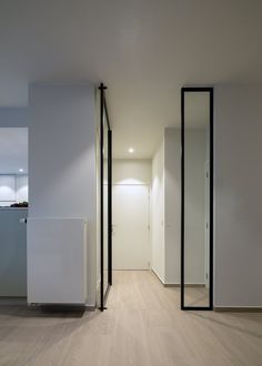 an empty room with white walls and wood flooring is seen from the hallway to the kitchen