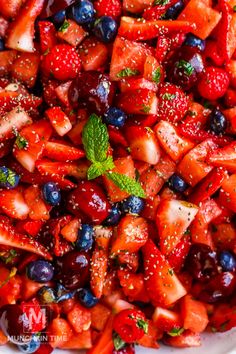 strawberries and blueberries are mixed together in a bowl with minty garnish