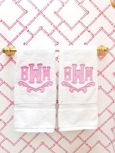 two white towels with pink embroidered monogrammed letters on them hanging from gold hooks