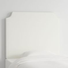 a white headboard on a bed with sheets and pillows in the corner, against a plain white wall