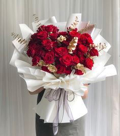 a woman holding a bouquet of red roses in her hands with gold accents on it