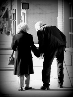 an old man and woman holding hands on the sidewalk