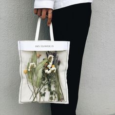 a person holding a white bag with flowers on the front and side, in front of a grey wall