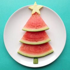 a watermelon christmas tree cut into slices on a white plate against a blue background