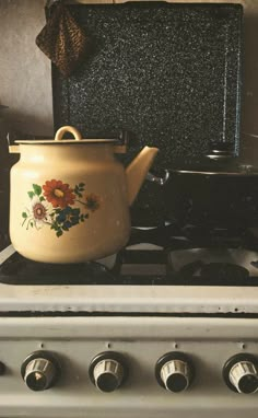 a tea pot sitting on top of a stove next to a frying pan with flowers painted on it