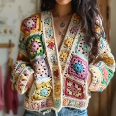 a woman wearing a colorful crochet jacket and jeans standing in front of a wall