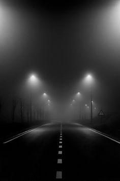 an empty road with street lights in the fog