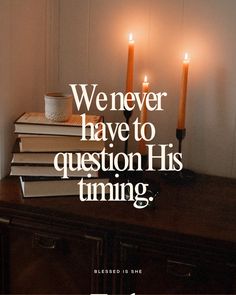 a stack of books sitting on top of a wooden table next to two lit candles