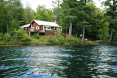 a house sitting on top of a lush green forest next to a lake filled with water