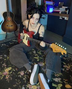 a woman sitting on the floor with two guitars in front of her and one guitar behind her