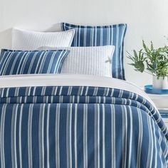 a bed with blue and white striped bedspread next to a potted plant