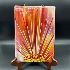 an art glass sculpture with yellow and red sticks in it's center on a wooden stand