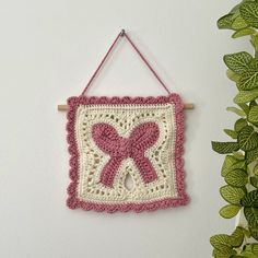 a pink and white crocheted wall hanging with a bow on it's side