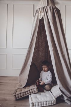 a little boy sitting in a teepee tent with pillows on the floor next to it