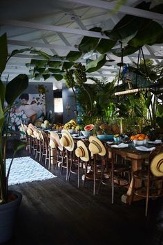 a long table with chairs and plates on it in a room filled with tropical plants