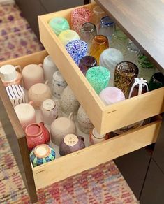 an open drawer filled with vases on top of a wooden table next to a rug