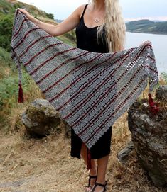 a woman holding up a crocheted shawl in front of a body of water